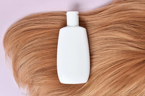 White shampoo bottle on blonde hair with pink background