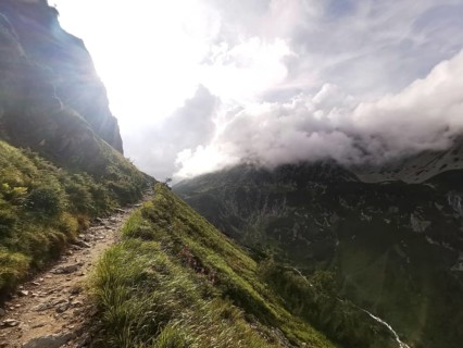 An illuminated mountain trail with dramatic backlight leads through a mountainous landscape, hiking