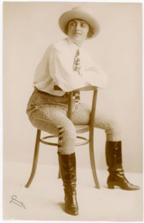 Elegant, self-confident woman in pants, boots, in 1920s clothing sitting on a chair, black and