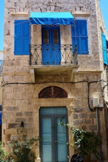 A traditional stone house with blue shutters and a small balcony, Pothia, main town, port,
