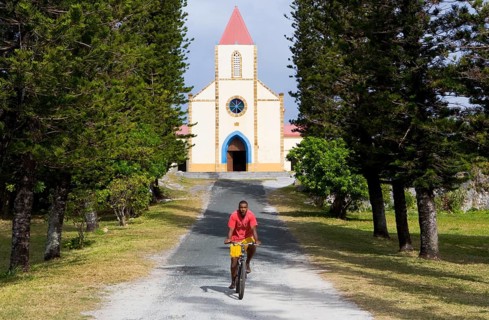 A cyclist rides along the tree-lined avenue in front of St Joseph's Church, Ouvea, New Caledonia