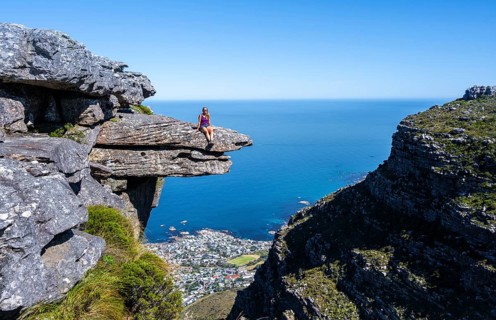 Young woman sitting on an imposing rock pin on a cliff, view of sea and coast, Kasteelspoort