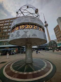 The world clock on Alexanderplatz with the Berlin television tower in the distance on an overcast