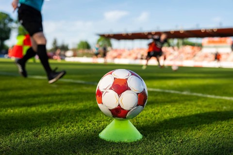 Soccer ball on a training cone near the touchline during a football match with players and stadium