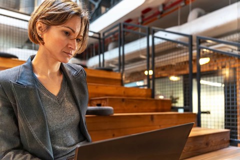 Professional woman in blazer with laptop on wooden steps in coworking space