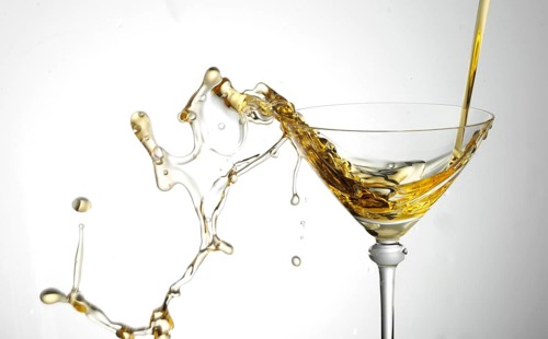A strong flood of golden yellow liquid pours into a cocktail glass and spills over, studio shot
