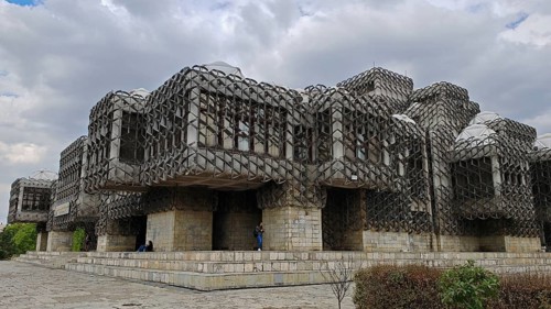 Modern building, National Library, Pjeter Bogdani, with unique stone grid design under cloudy sky,
