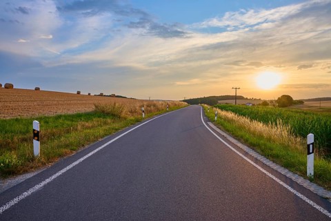 A country road that snakes through the fields as the sun sets on the horizon, summer,