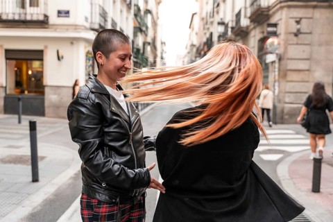 A lesbian couple enjoys a carefree moment on a city street, with one partner smiling brightly as