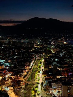 Nighttime cityscape with river, bridges and illuminated roads, hills in the background and dark