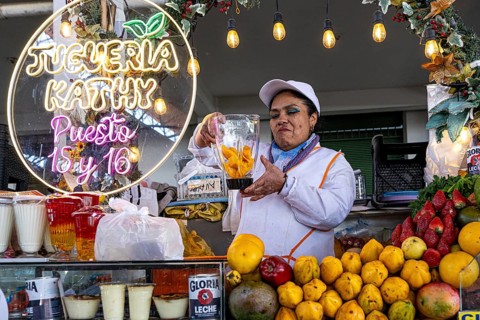 A friendly smiling woman from the indigenous population prepares fresh fruit juice behind a stand