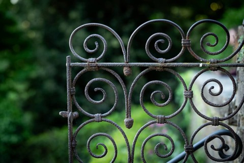 Close-up view of a rusty iron gate with spirals against a blurred green background, Bardini Garden