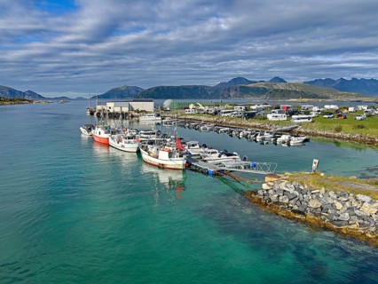 Several boats are moored on a quay in a picturesque harbor with caravans and mountains in the