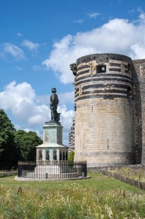 Bronze statue of King René on a decorated stone base in the foreground in front of one of the