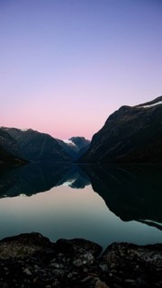 A calm lake reflects the surrounding mountains at sunset, under a pink sky, evening mood on the