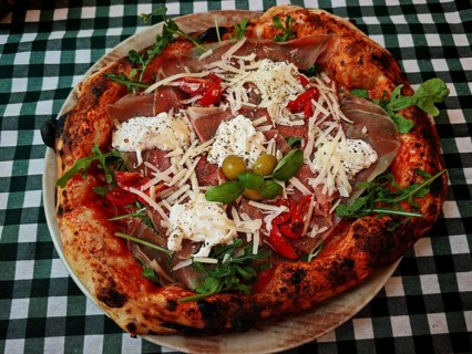 A richly topped pizza with ham, cheese and vegetables on a checkered tablecloth, Croatia