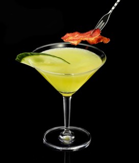 Yellow-green cocktail with black background, cucumber slice and ham as garnish, studio shot