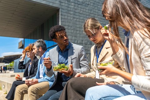 Diverse business colleagues are enjoying a healthy lunch together, sitting outside a modern