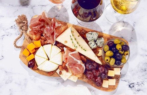 A cheese and charcuterie board displays different types of cheese and meats. The setting is a