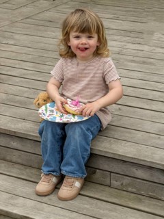 Little Caucasian girl, 3 years old, sitting on a wooden deck and eating a cake in Ystad, Skåne