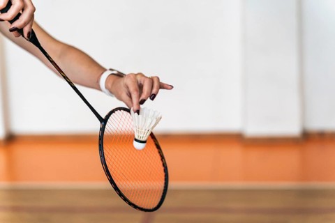 A close-up view of a woman preparing to serve in an indoor badminton court. The frame focuses