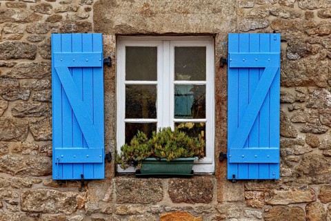 Stone wall with a window framed by blue shutters. Including a flower pot with succulents, blue