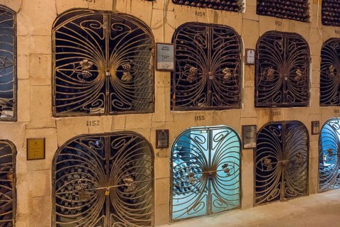 Rows of bottle racks with metal mesh doors showing a secure wine storage location in a cellar, wine