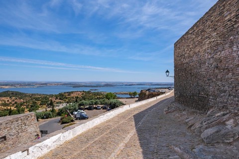 Stone path with view of lake and blue sky, stone wall on the right, rustic atmosphere, Monsaraz,