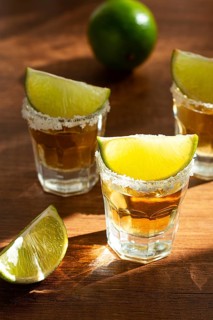 Three glasses with tequila and salt on the rims are arranged on a wooden table. Each glass has a