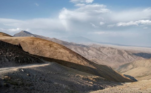 Mountain pass at Songköl, gravel road at a plateau, mountains in the background, Kyrgyzstan