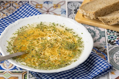 Ready made soup with noodles in a white plate next to bread