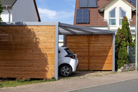 Beautiful carport made of wood and metal with side slatted walls and a fixed roof next to a