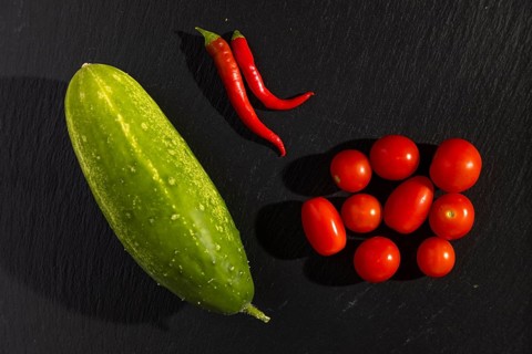 A cucumber, two red chili peppers tomatoes on a dark background