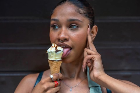 Young woman with a septum piercing enjoying a sweet dessert, licking a melting ice cream cone with
