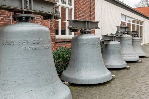 Row of grey bells in front of an outdoor brick building on stone pavement, Gescher Bell Museum,