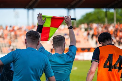 Assistant referee holding a flag during a soccer match while officials and substitute players stand