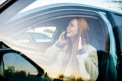 A beautiful pregnant girl with striking red hair is seated in her car, joyfully talking on her