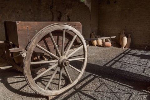 Old wooden cart and ceramic jugs on display inside an unenclosed building at the ancient ruins of