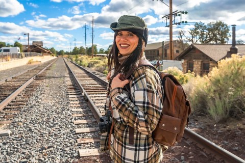 Woman standing on the railroad tracks near the grand canyon depot, wearing a plaid shirt and hat,