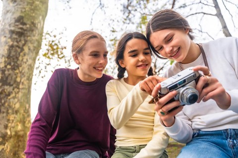 Three happy young siblings spending time outdoors in a park, eagerly looking at a vintage camera