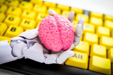 Robotic hand holding a brain in front of a computer keyboard, symbolic photo artificial