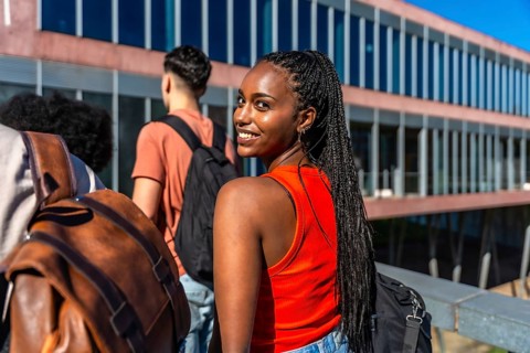 Smiling young black student looking back while walking with friends on university campus,