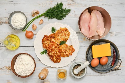 Raw ingredients surrounding plate with fried chicken patties. Raw chicken fillets, onion, eggs,