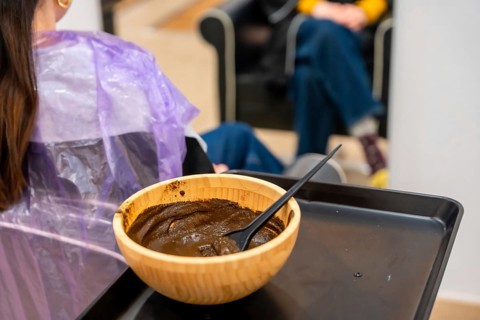 Customer receiving a natural hair coloring application with henna paste from a wooden bowl,