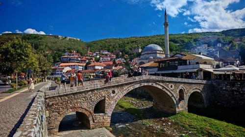 Urban scene with tourists on bridge over Prizren Bristrica river, mosque in background and hills