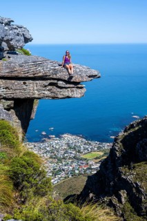 Young woman sitting on an imposing rock pin on a cliff, view of sea and coast, Kasteelspoort