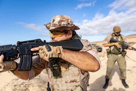 Two soldiers in tactical gear engage in a training exercise in a desert setting. They are focused