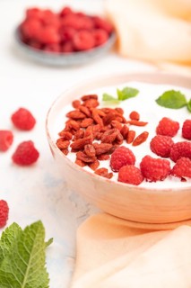 Yogurt with raspberry and goji berries in ceramic bowl on white concrete background and orange