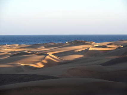 Sunlight creates dramatic shadows on dunes in front of the sea, Maspalomas Dunes, Gran Canaria,