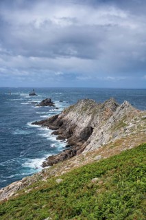 Steeply sloping, rocky cliffs of the Breton coast under blue skies with light clouds. The view